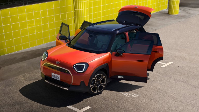 The first-ever all-electric MINI Aceman with all five doors open, including the boot. The car is stationary, parked by a yellow tiled wall.