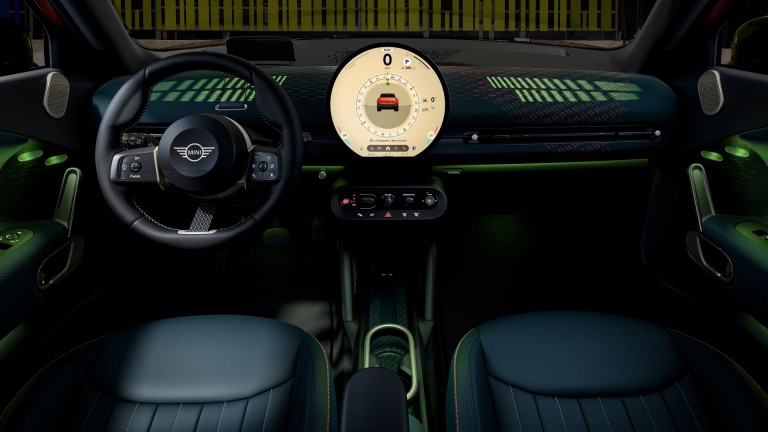 Backseat view of the new MINI Aceman’s upholstered front seats and illuminated knitted dashboard. The ambient lighting throughout is a result of the Experience Modes selected on the round OLED display.