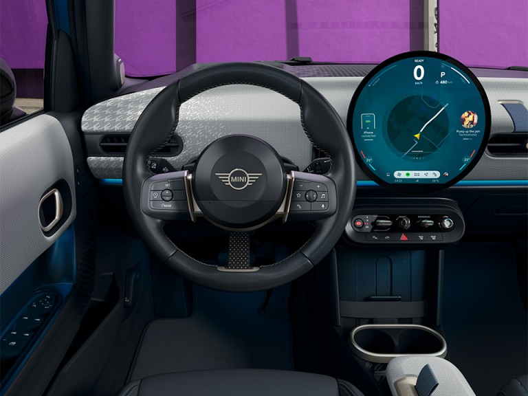 Close-up shot of the new MINI Cooper 5-Door’s steering wheel and round OLED display, taken from the drivers’ point of view.