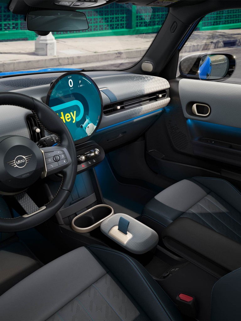 Interior view of the new MINI Cooper 5-Door, including the steering wheel, round OLED display, and 2D-knit dashboard.