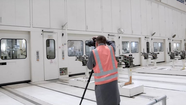 Video of Alastair Philip Wiper in an orange high-vis safety vest as he photographs a series of white factory doors.