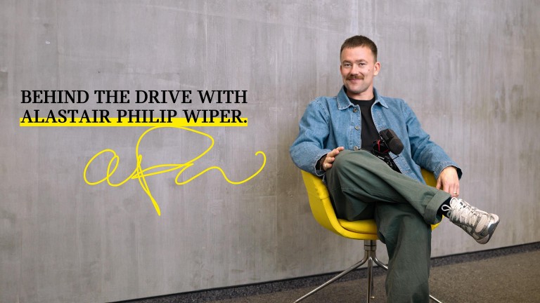 British photographer Alastair Philip Wiper sits with a camera on his lap and smiles for the photo.